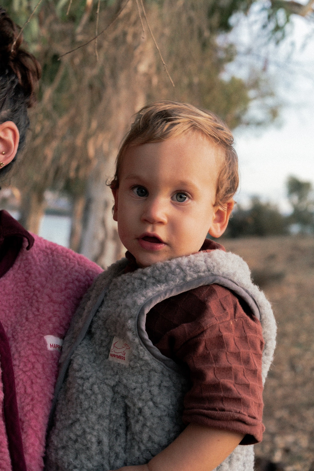 Child wearing a gray merino wool vest held by an adult outdoors