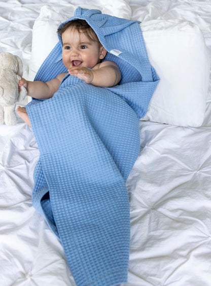 Baby wrapped in a blue swaddle on a white bed