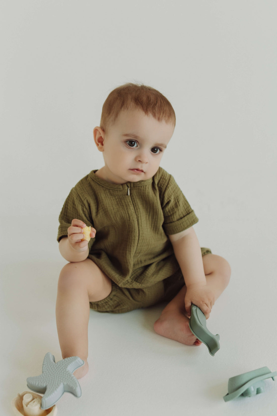 Baby in a green outfit sitting on a white floor with green toys.