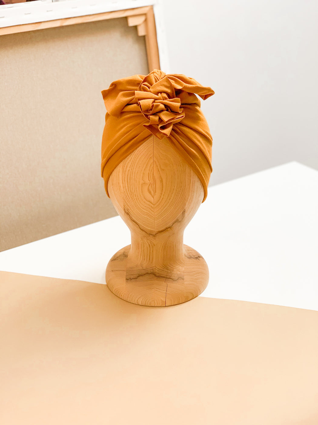 A mustrad turban for kids on a wooden mannequin standing on a beige white counter