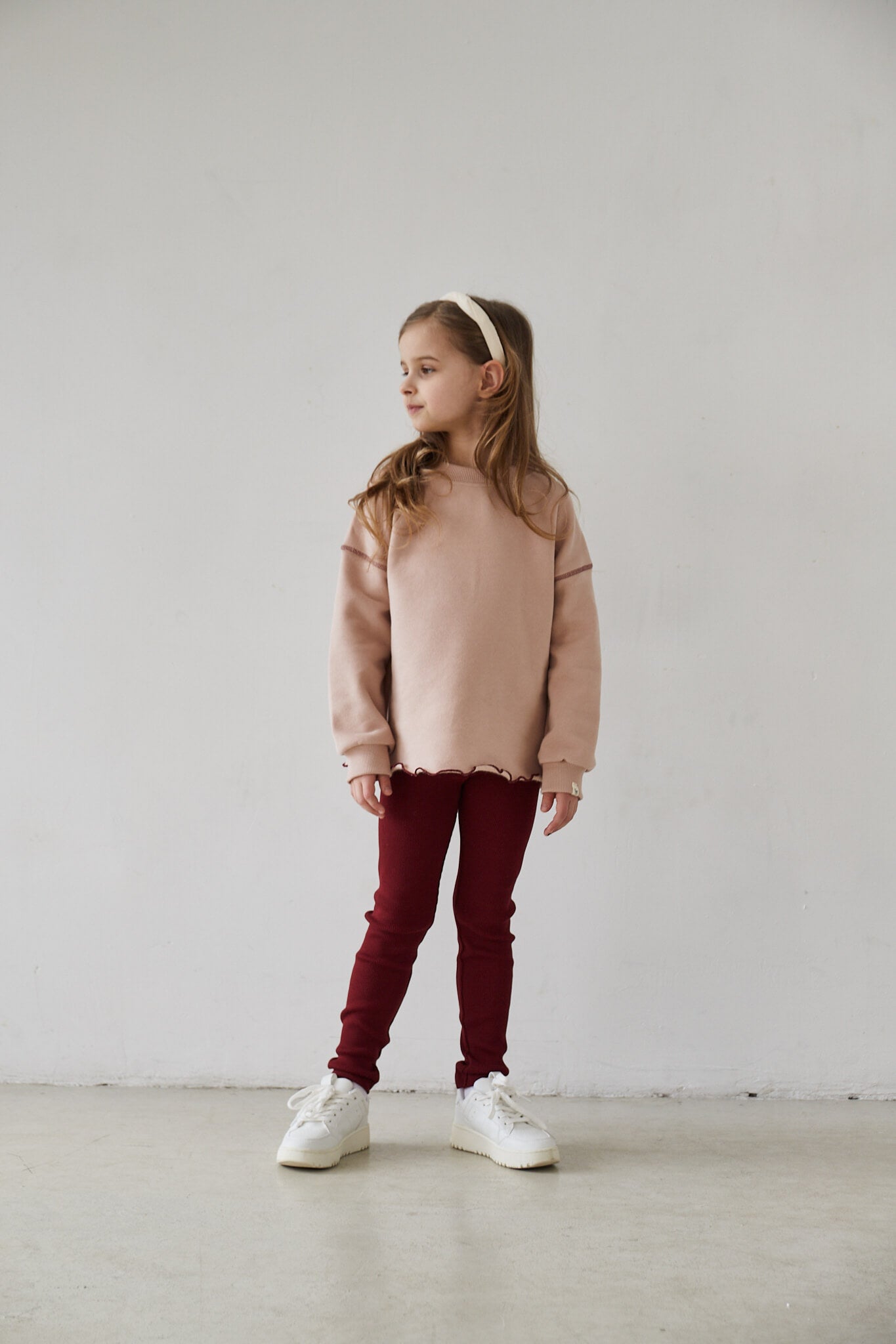 Girl wearing pink sweatshirt and red leggings smiling to the camera on a white background