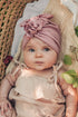 a small cute baby wearing a beige romper and pink turban in a moses basket