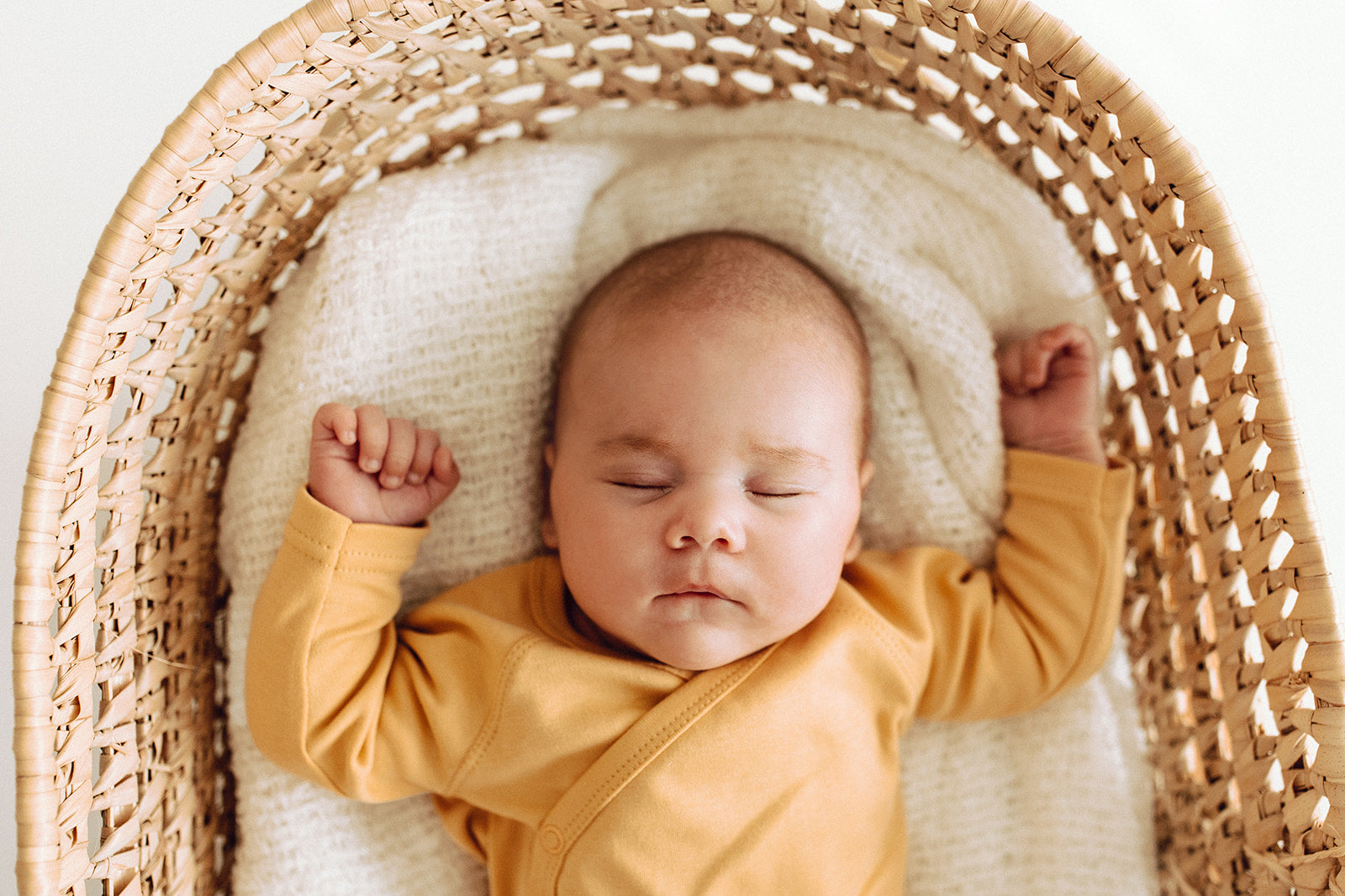 small sleeping baby in moses basket wearing organic cotton wrap style bodysuit