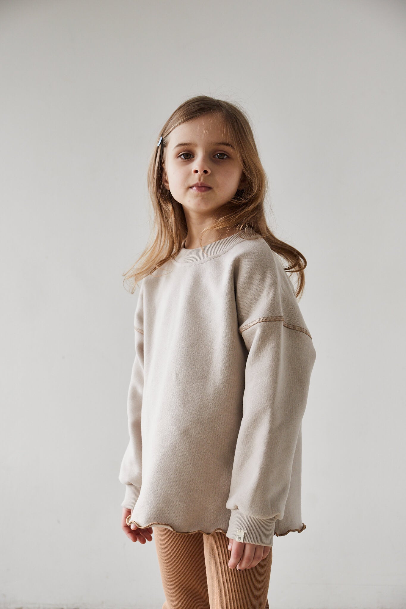 Girl wearing beige sweatshirt and brown leggings on a white background