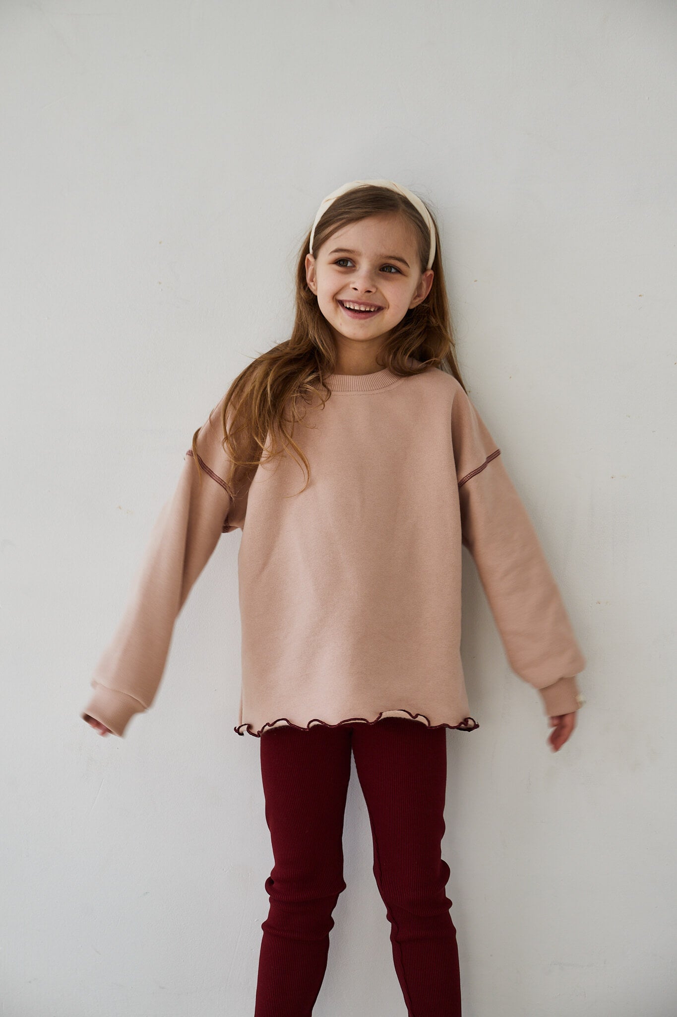 Girl wearing pink sweatshirt and red leggings smiling to the camera on a white background