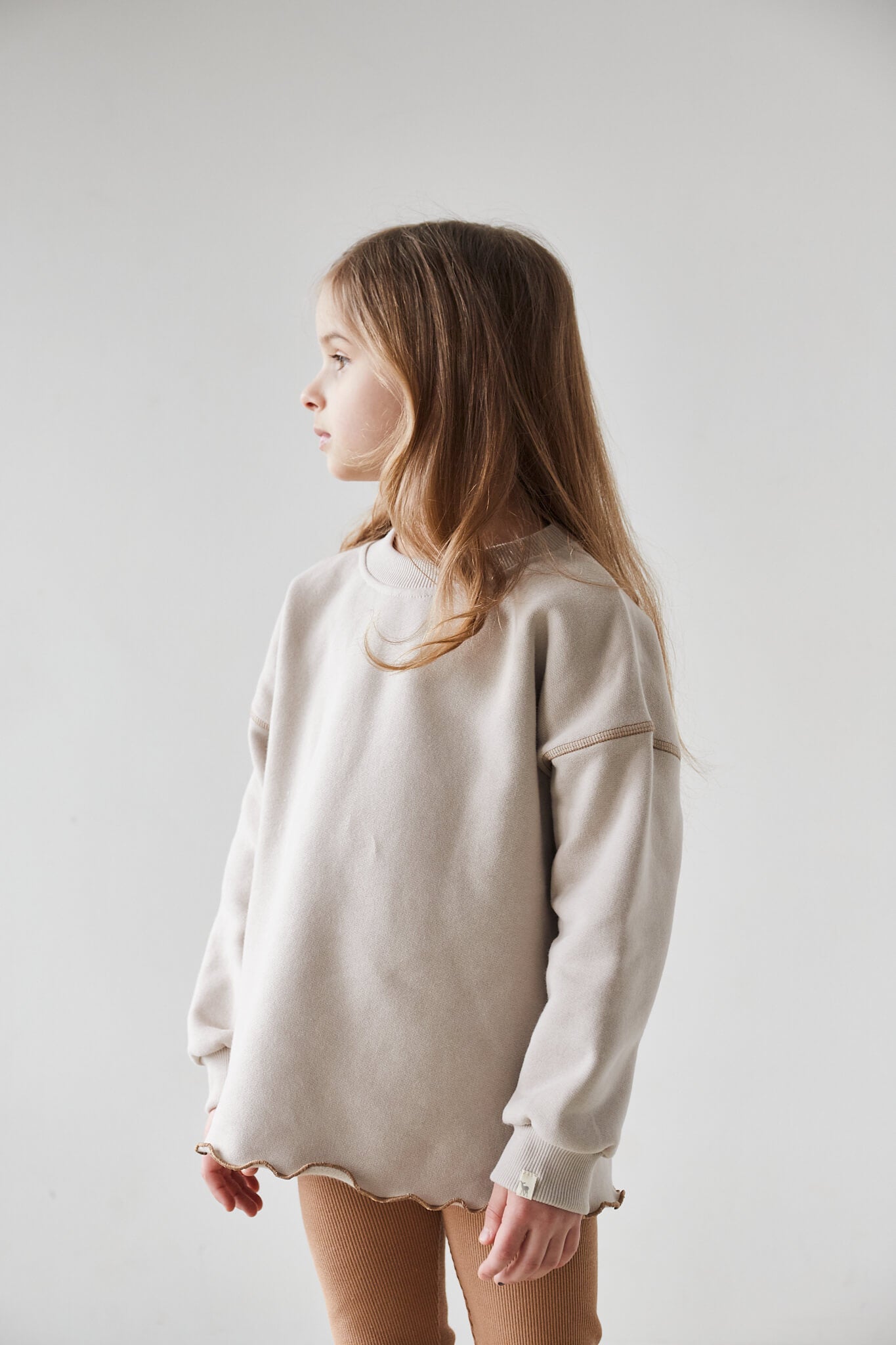 Girl wearing beige sweatshirt and brown leggings on a white background