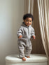 Baby in a taupe merino overall standing on a ivory chair