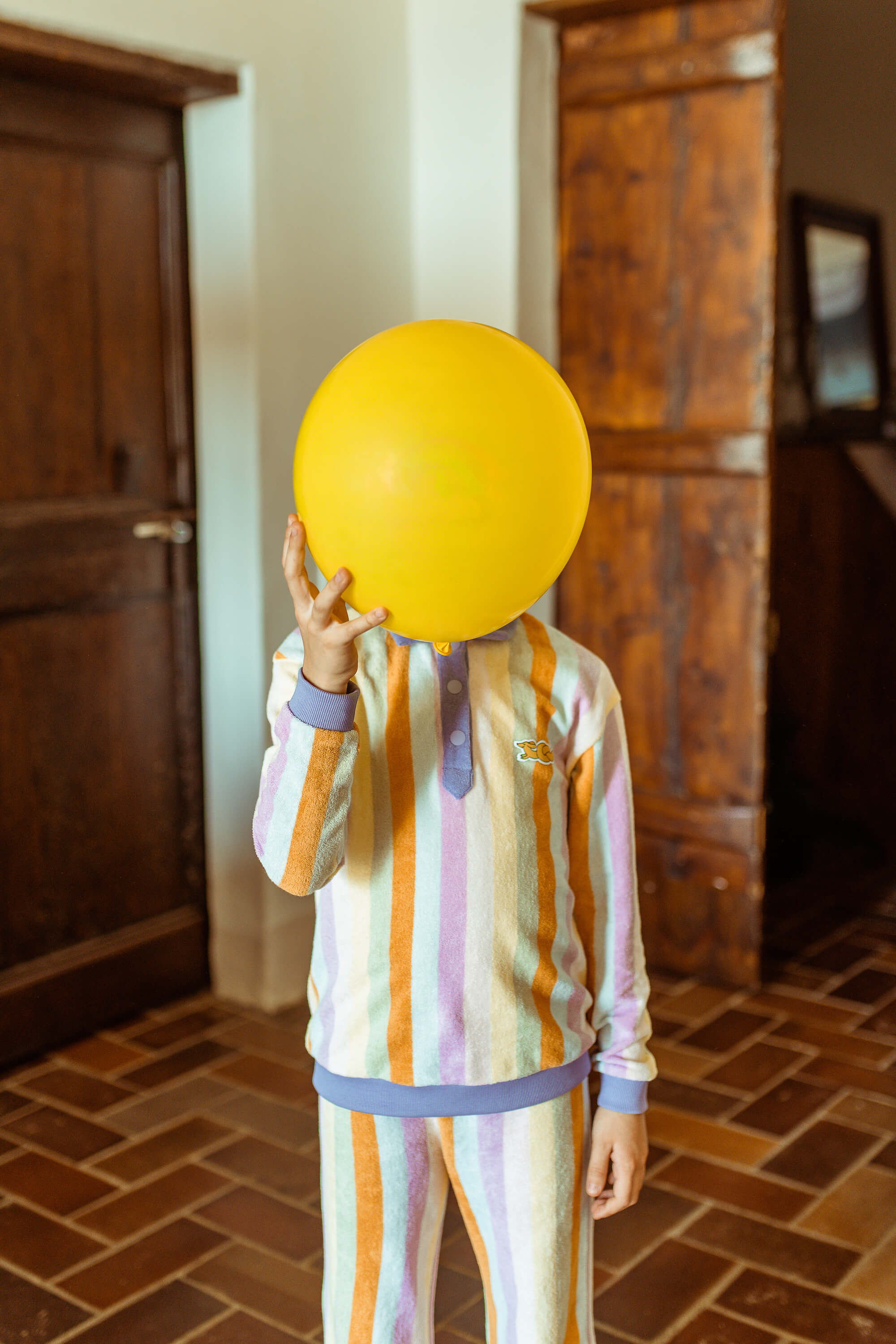 Child wearing a striped long-sleeve terry sweatshirt in multiple colors, with a yellow baloon covering the head