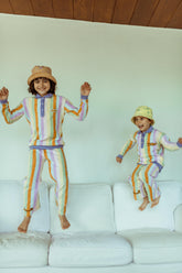 Two children in matching colorful outfits jumping on a white couch.