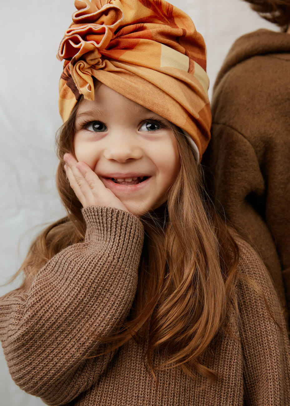 Ein kleines Mädchen angezogen in Baumwolle Turban und braunen Pullover