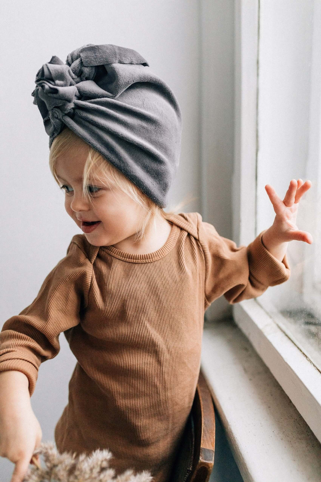 A girl wearing brown ribbed bodysuit and grey turban standing at the window