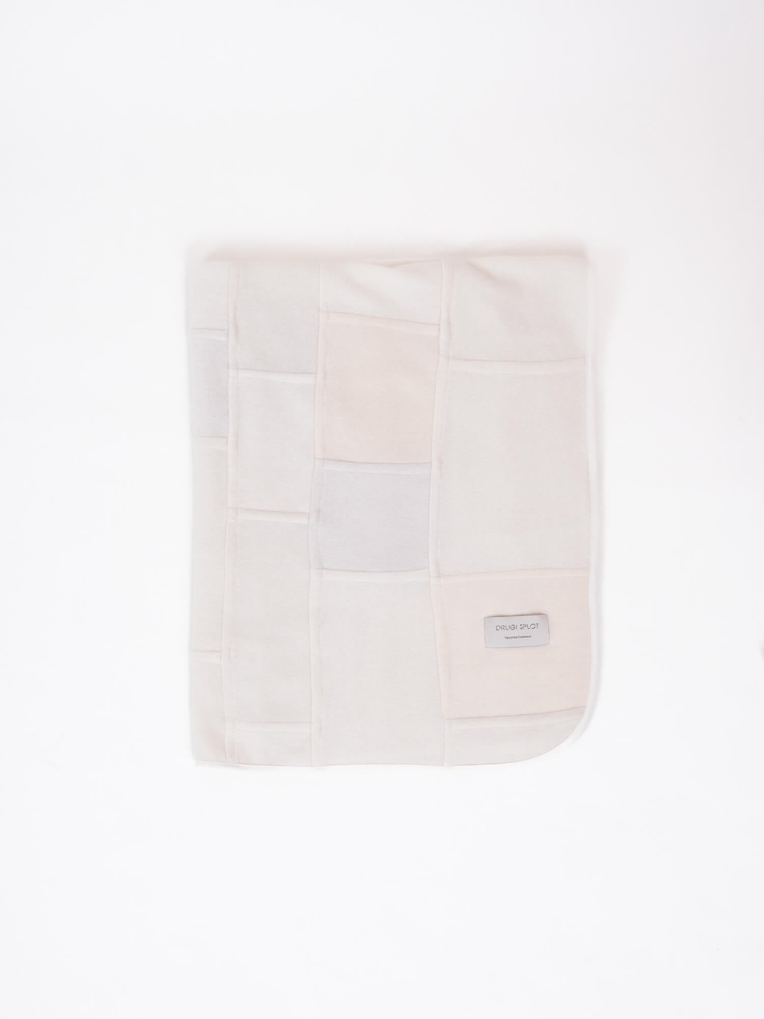 A patchwork blanket with rectangles in shades of white, ecru and beige laid out on a white background.