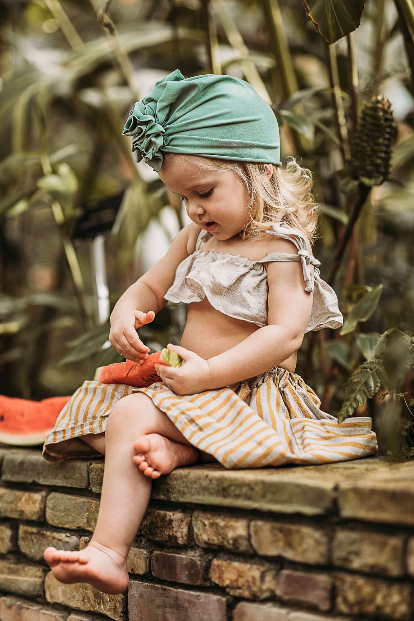 a small blonde girl eating a watermelon and wearing a vintage mint turban