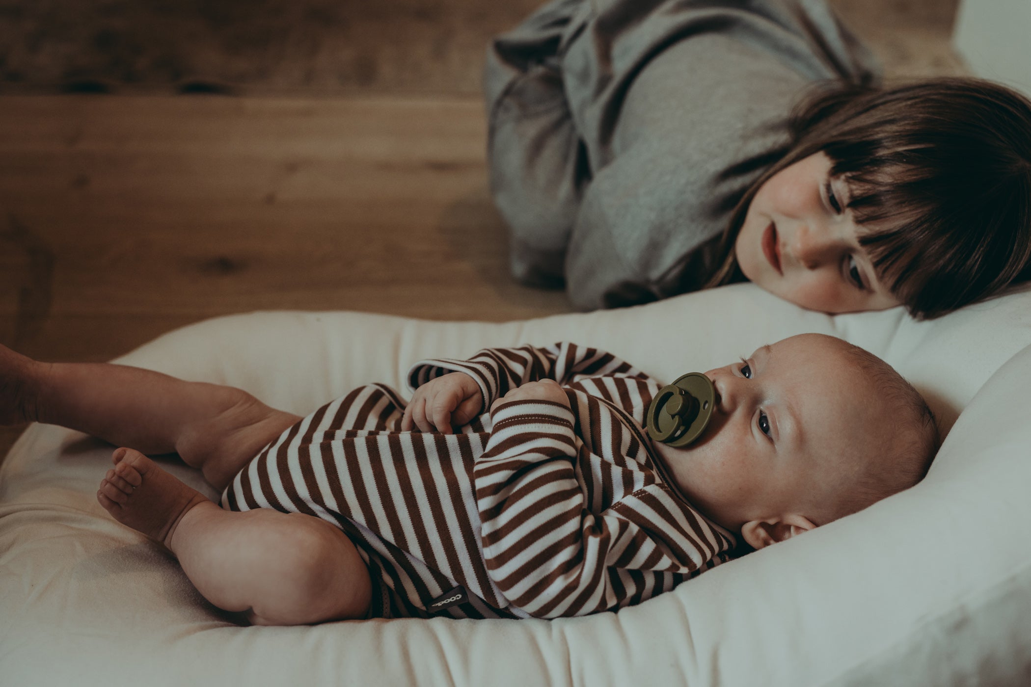 Newborn resting on cushion in striped organic cotton romper